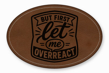 An oval brown leather patch with white stitched edges and black text reading BUT FIRST let me OVERREACT.