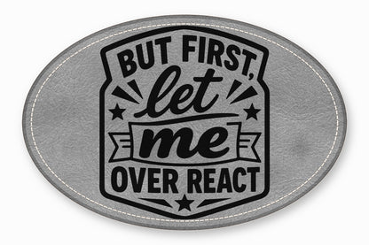 An oval gray faux leather patch with white stitched edges and black text reading "BUT FIRST, let me OVER REACT".
