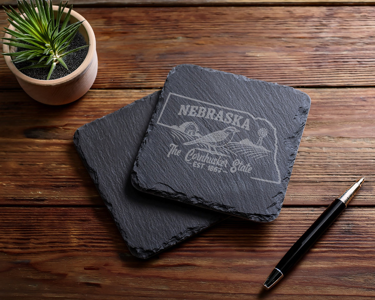 Nebraska state outline coasters with bird and windmill design, on wooden surface.
