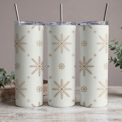 Three white tumblers with gold snowflake pattern and metal straws on a wooden surface.