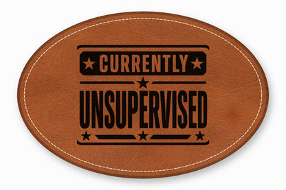 An oval brown leather patch featuring white decorative stitching and the black text currently unsupervised.