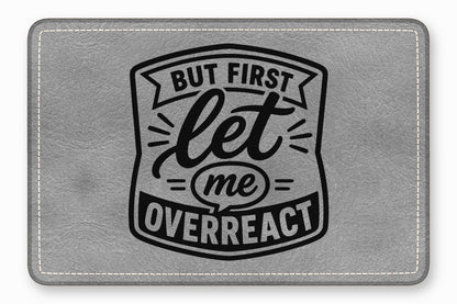 Gray leatherette patch with rounded corners, white stitching, and black engraved text reading But First Let Me Overreact.