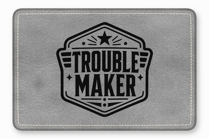 Gray leather patch with white stitched borders and a black emblem featuring the text Trouble Maker.
