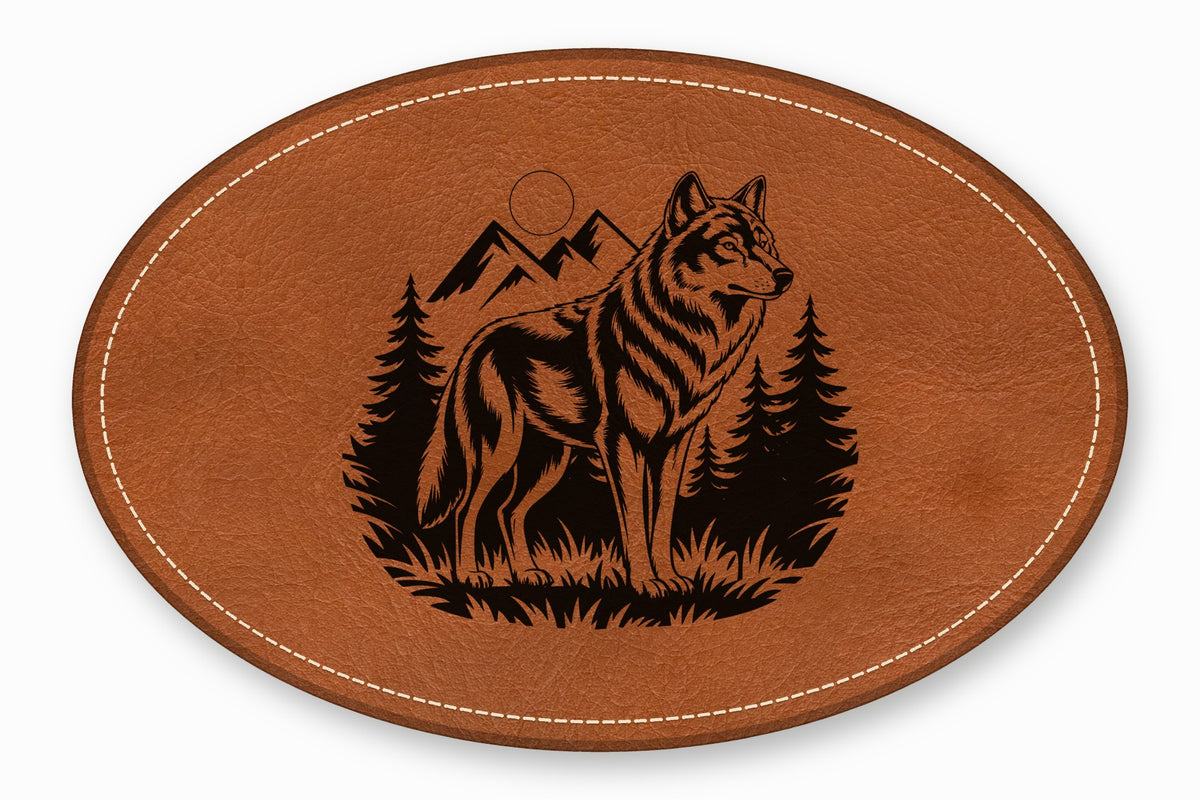 An oval brown leather patch featuring a laser-engraved design of a wolf standing before mountains and pine trees.