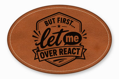 An oval brown leather patch with white stitched borders and black text reading But First let me OVER REACT.