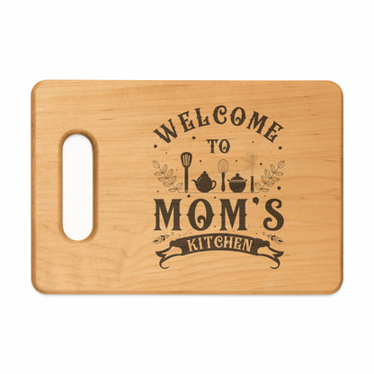 Wooden cutting board with "Welcome To Mom's Kitchen" engraved in dark lettering.