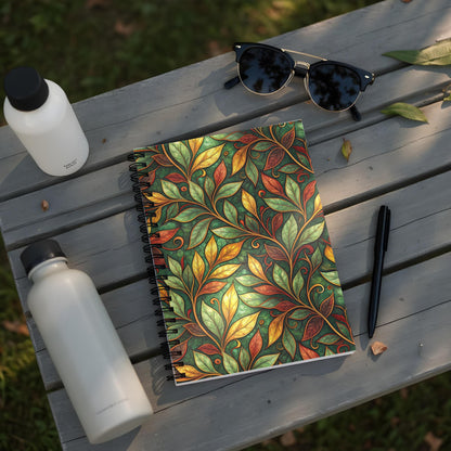 Notebook with green, yellow, and red leaf pattern on a wooden table with water bottles and sunglasses.