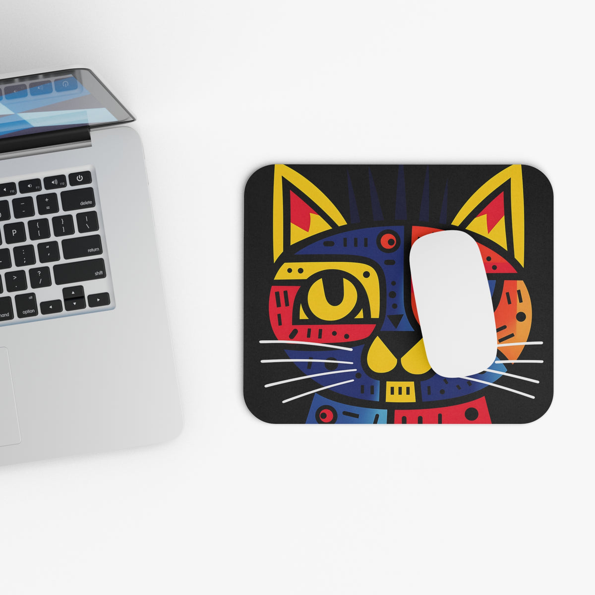 A colorful, abstract cat mousepad on a white desk beside a laptop with a white mouse on top.
