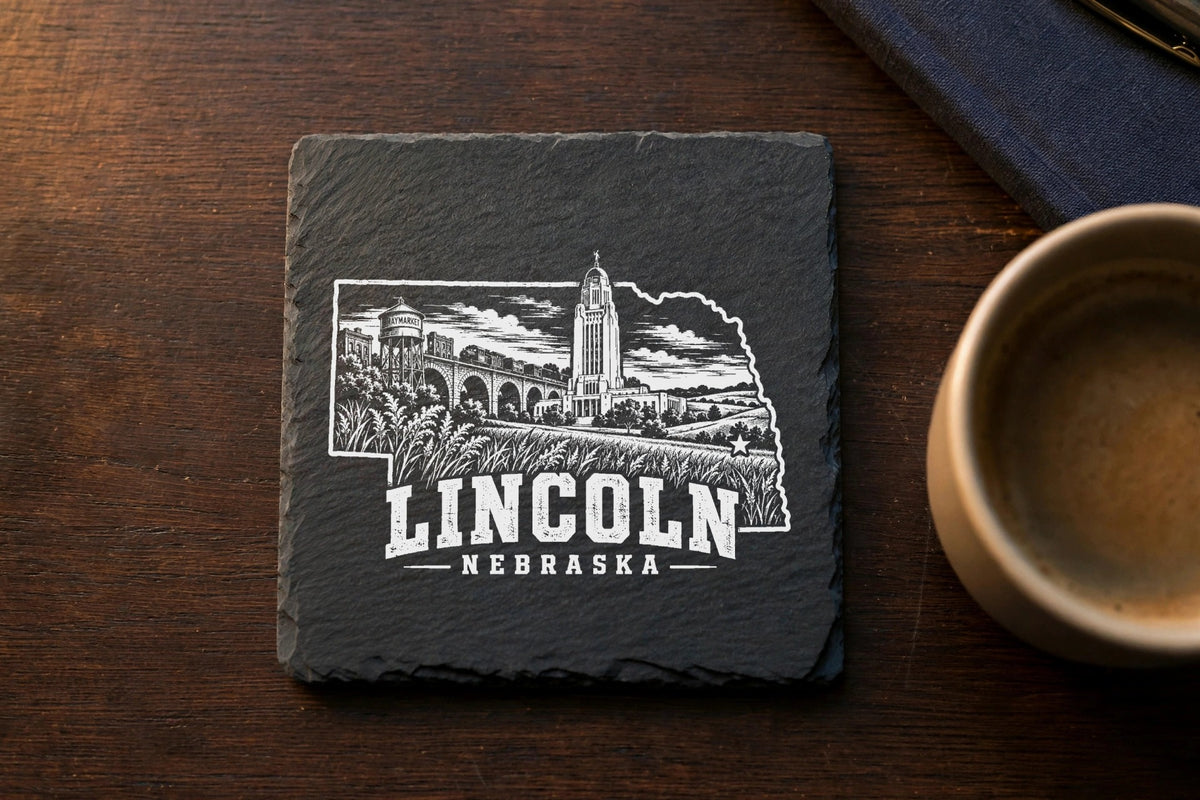 Square black slate coaster engraved with an outline of Nebraska featuring Lincoln landmarks and text.