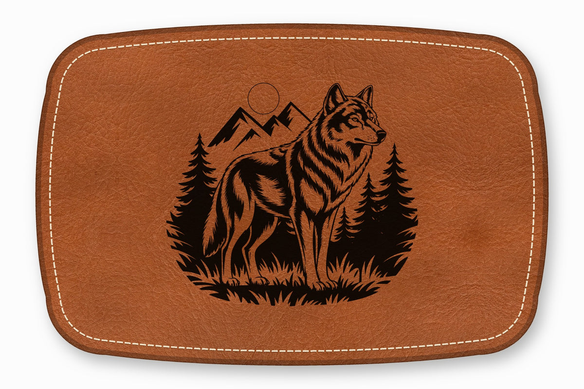 Brown leather rectangular patch with white stitched border and laser-engraved wolf, mountains, and pine trees.
