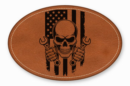 An oval brown leather patch featuring a skull holding wrenches over a distressed American flag design.