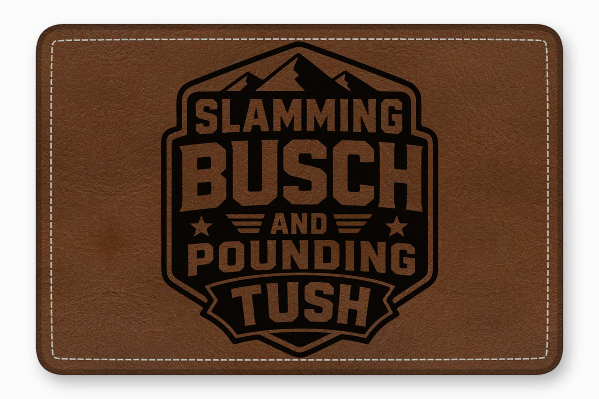 A rectangular brown leather patch with white stitched borders and a black laser-engraved mountain emblem reading Slamming Busch and Pounding Tush.