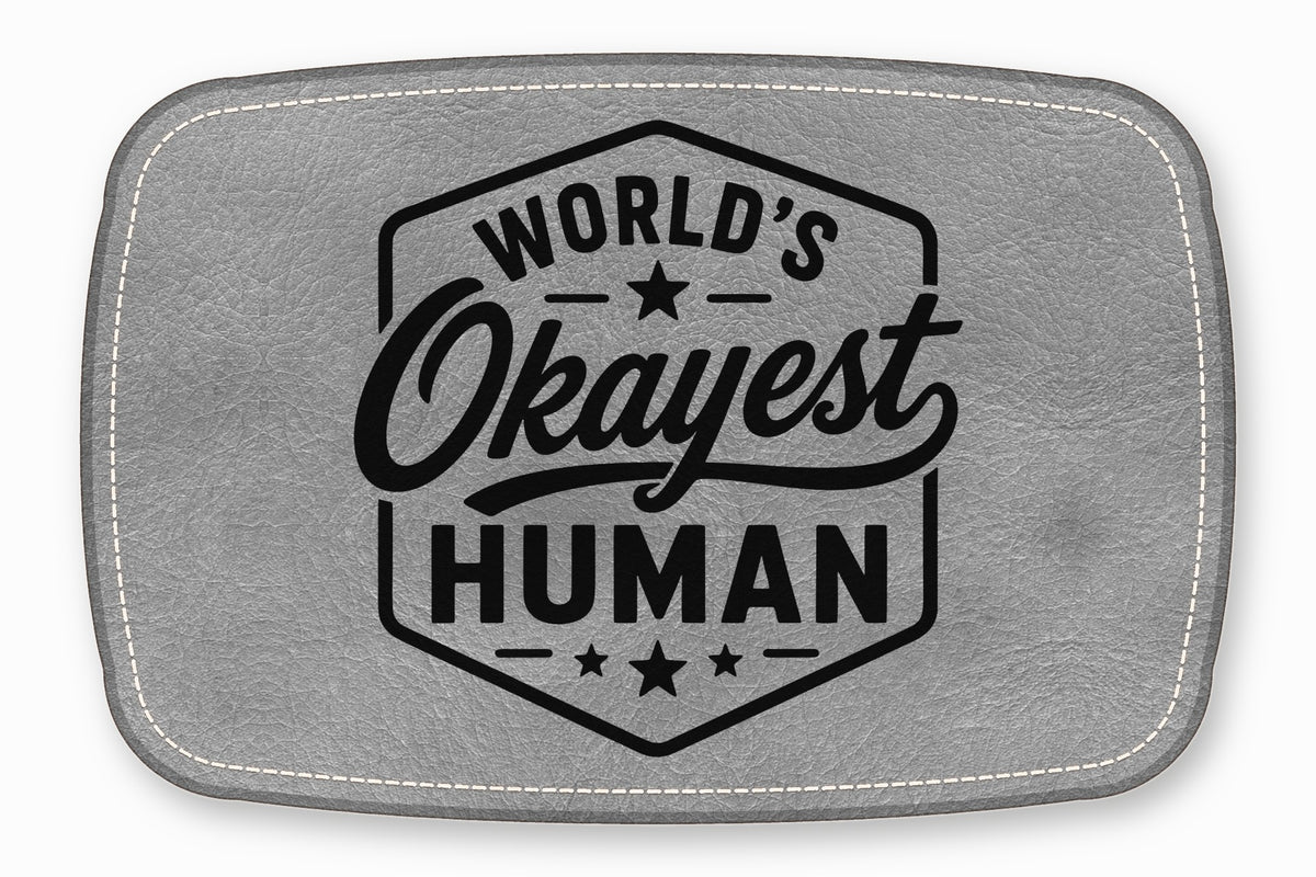 Gray leather patch with rounded corners, white stitching, and the black text "WORLD'S OKAYEST HUMAN."