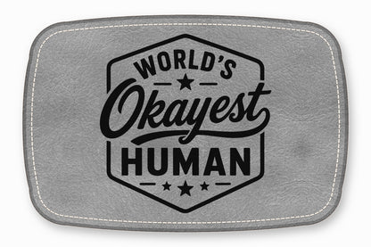Gray leather patch with rounded corners, white stitching, and the black text "WORLD'S OKAYEST HUMAN."