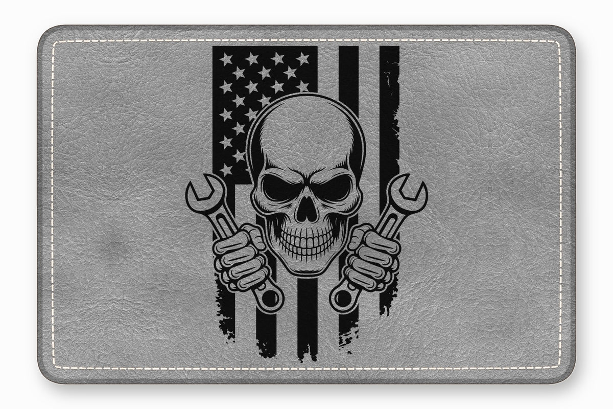 Grey leather patch featuring a black graphic of a skull holding two wrenches over an American flag.