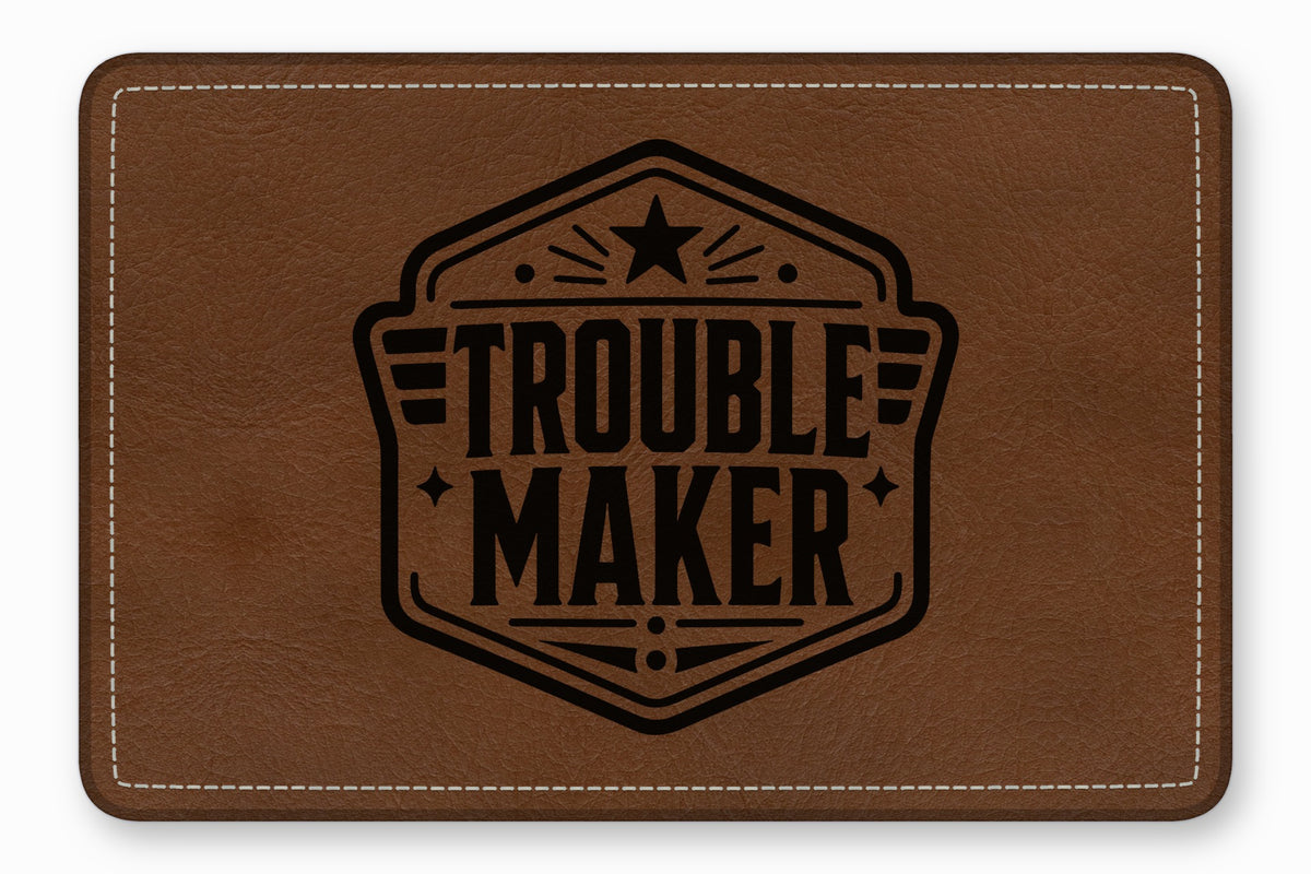 Brown leather rectangular patch with white stitched borders and a black printed emblem reading "TROUBLEMAKER."