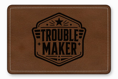 Brown leather rectangular patch with white stitched borders and a black printed emblem reading "TROUBLEMAKER."