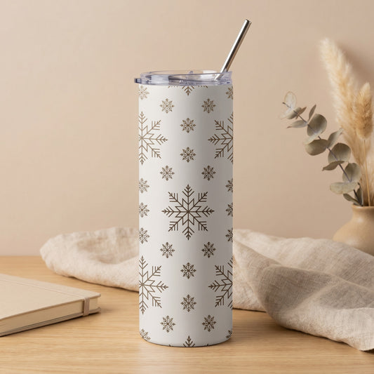 White tumbler with brown snowflake pattern and metal straw on a wooden surface.