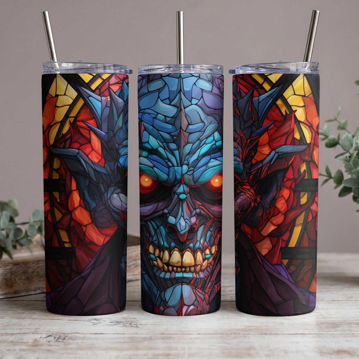 Three tumblers with a stained-glass demon face design and stainless steel straws.