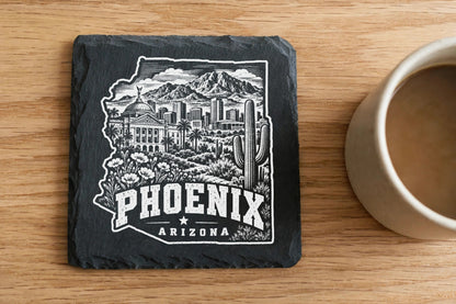 Black slate coaster featuring a white laser-engraved Phoenix, Arizona skyline design next to a coffee mug.