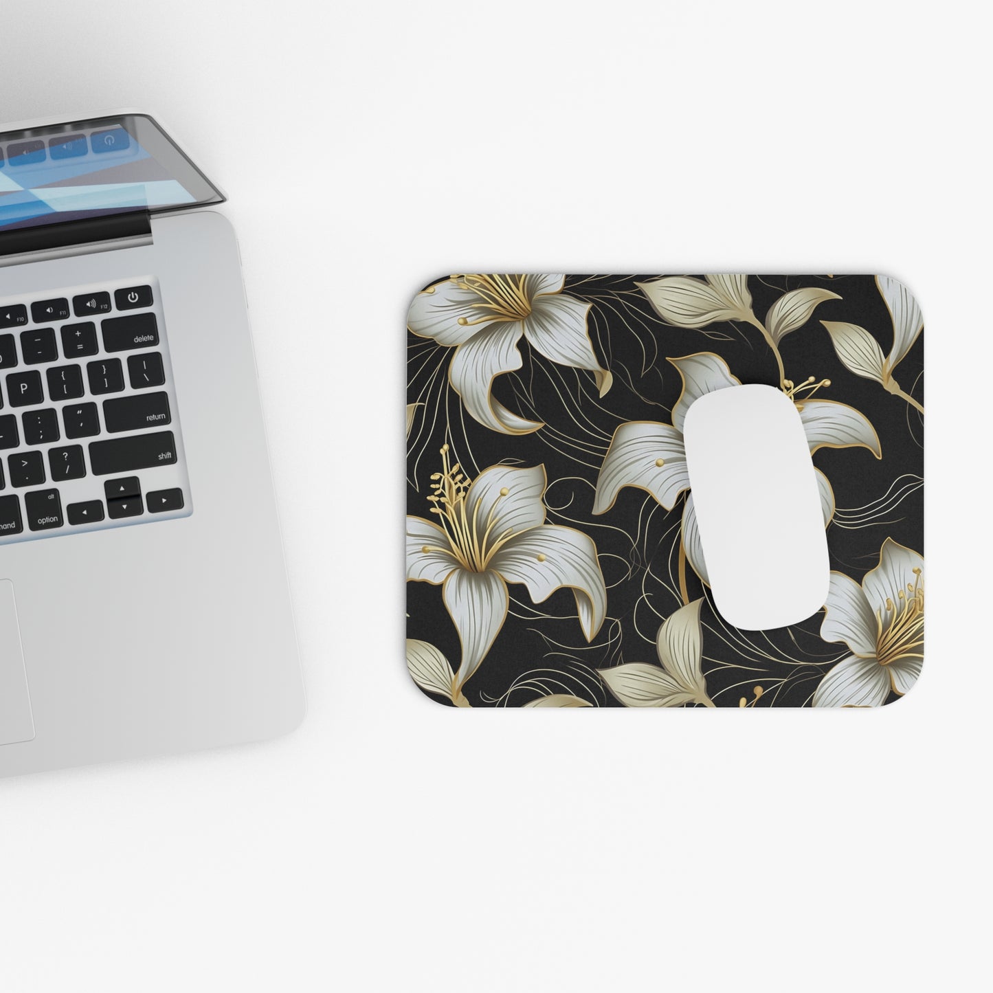 Mousepad with black background and white and gold floral design, beside a laptop.