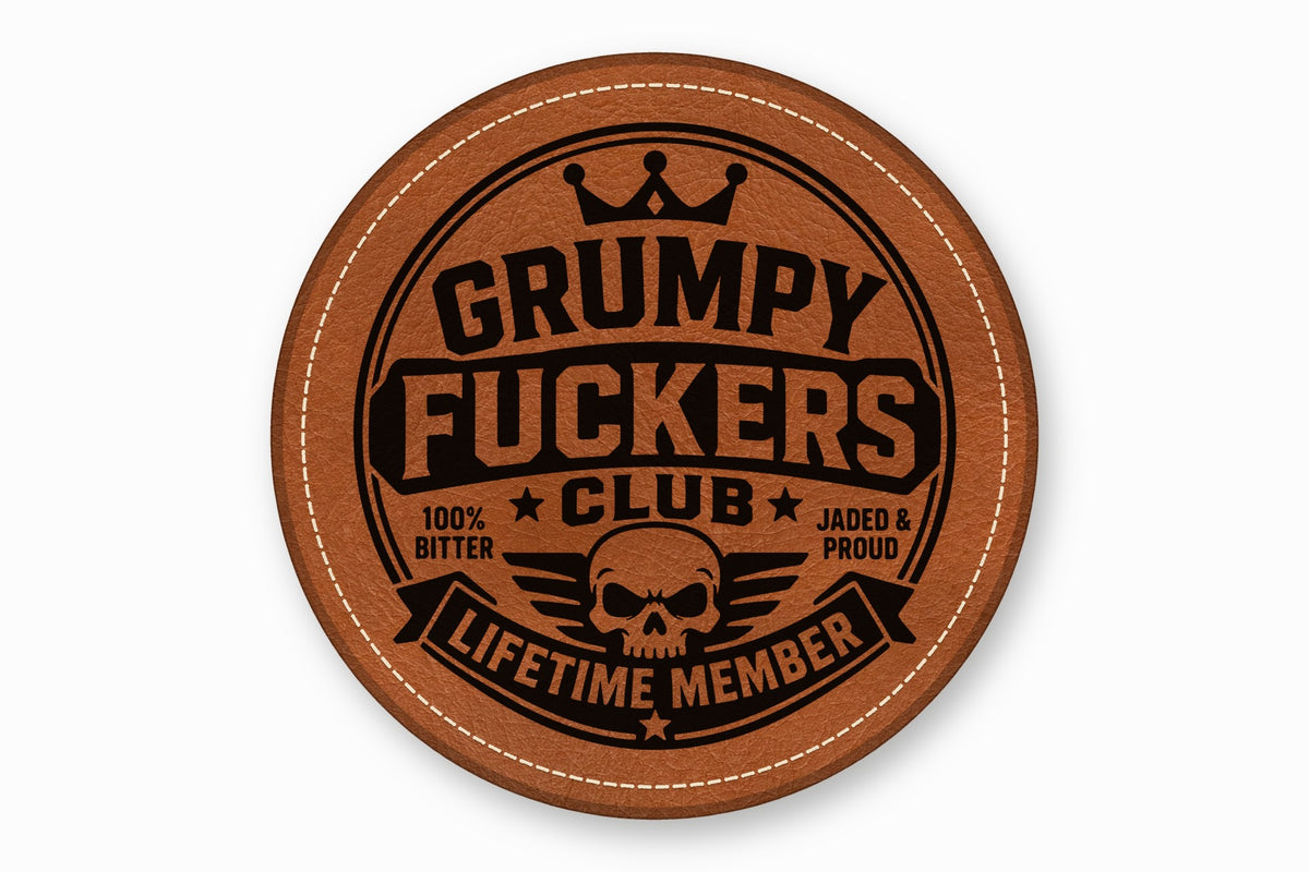 A round brown leather coaster with white stitched edges and a black skull graphic with text.
