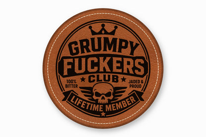 A round brown leather coaster with white stitched edges and a black skull graphic with text.