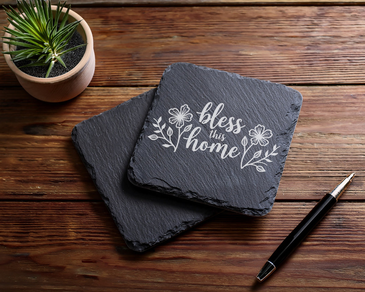 Two slate coasters with "bless this home" text and floral design.