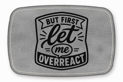 A gray faux leather patch with white stitched edges and black text reading But first let me overreact.