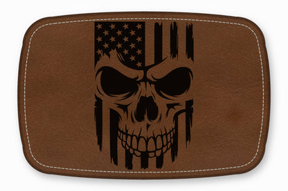 Brown rectangular leather patch with white stitched borders and a black engraved American flag skull design.