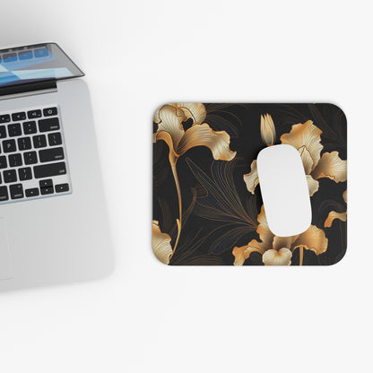 Black mousepad with gold iris floral design next to an open laptop.