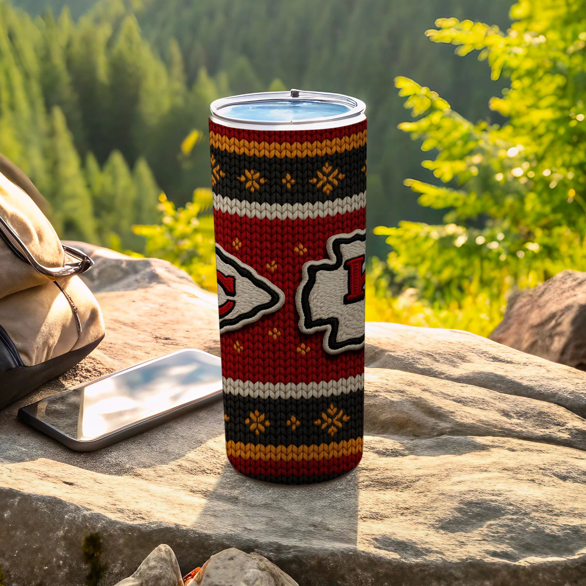 Kansas City Chiefs ugly sweater pattern tumbler with a smartphone and backpack outdoors.