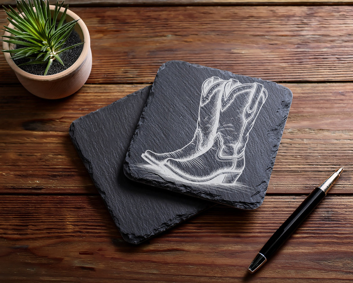 Slate coasters engraved with cowboy boots design, next to a plant and pen.