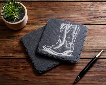 Slate coasters engraved with cowboy boots design, next to a plant and pen.