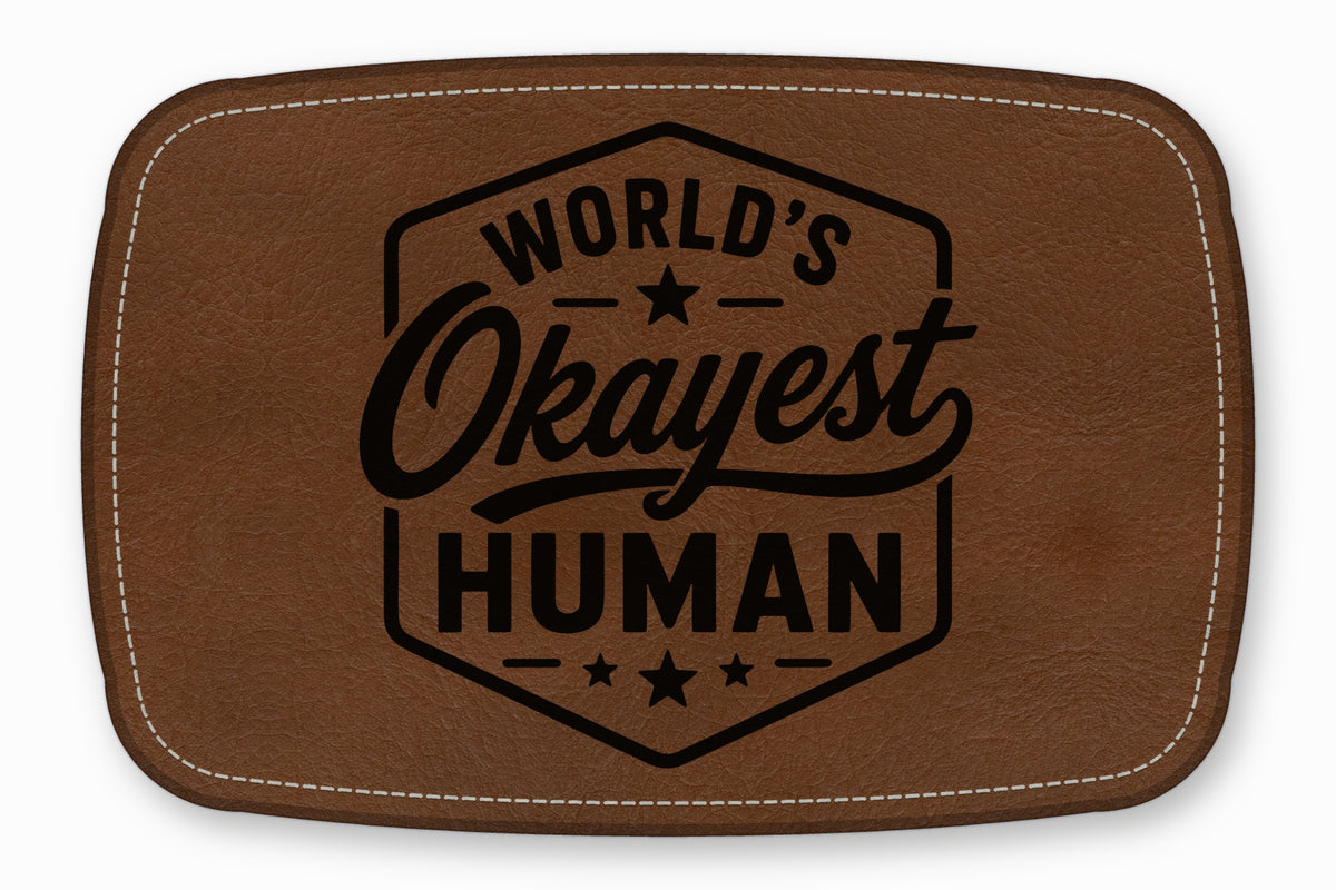 Brown rectangular leather patch with white stitched border, featuring the engraved text World's Okayest Human.