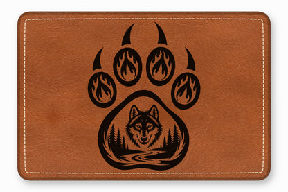 Brown leather patch featuring a black engraved bear paw print enclosing a forest landscape and wolf face.