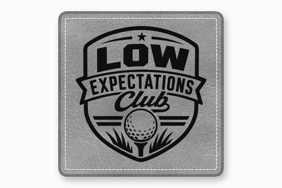 Square grey leather patch with white stitched border and a black golf-themed crest design reading Low Expectations Club.