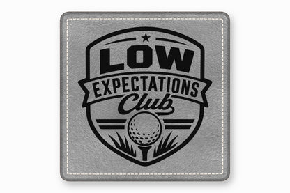 Square grey leather patch with white stitched border and a black golf-themed crest design reading Low Expectations Club.