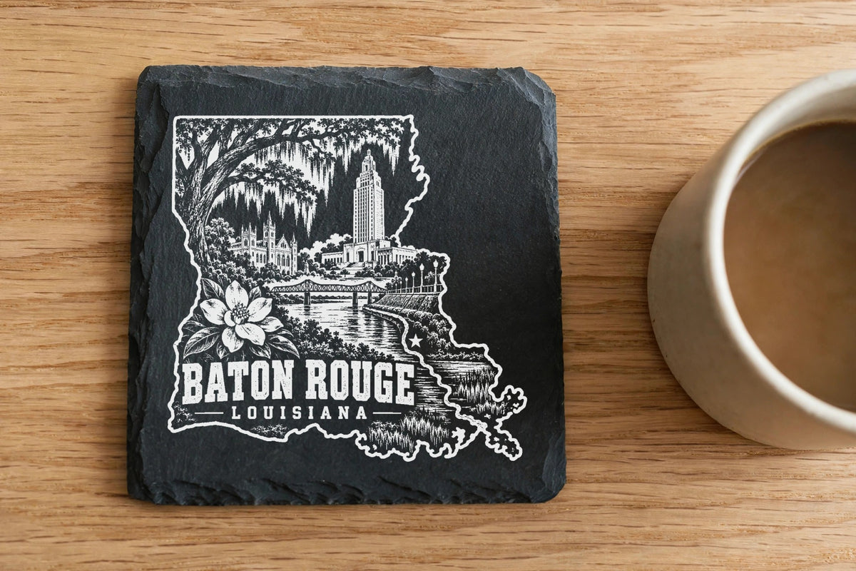 Square black slate coaster engraved with a Baton Rouge, Louisiana landmark design beside a coffee mug.