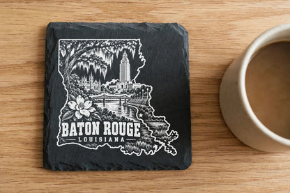 Square black slate coaster engraved with a Baton Rouge, Louisiana landmark design beside a coffee mug.