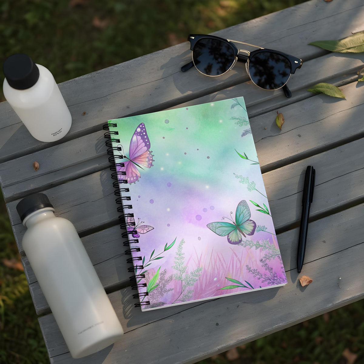 Spiral notebook with watercolor butterflies and greenery on purple and green background.