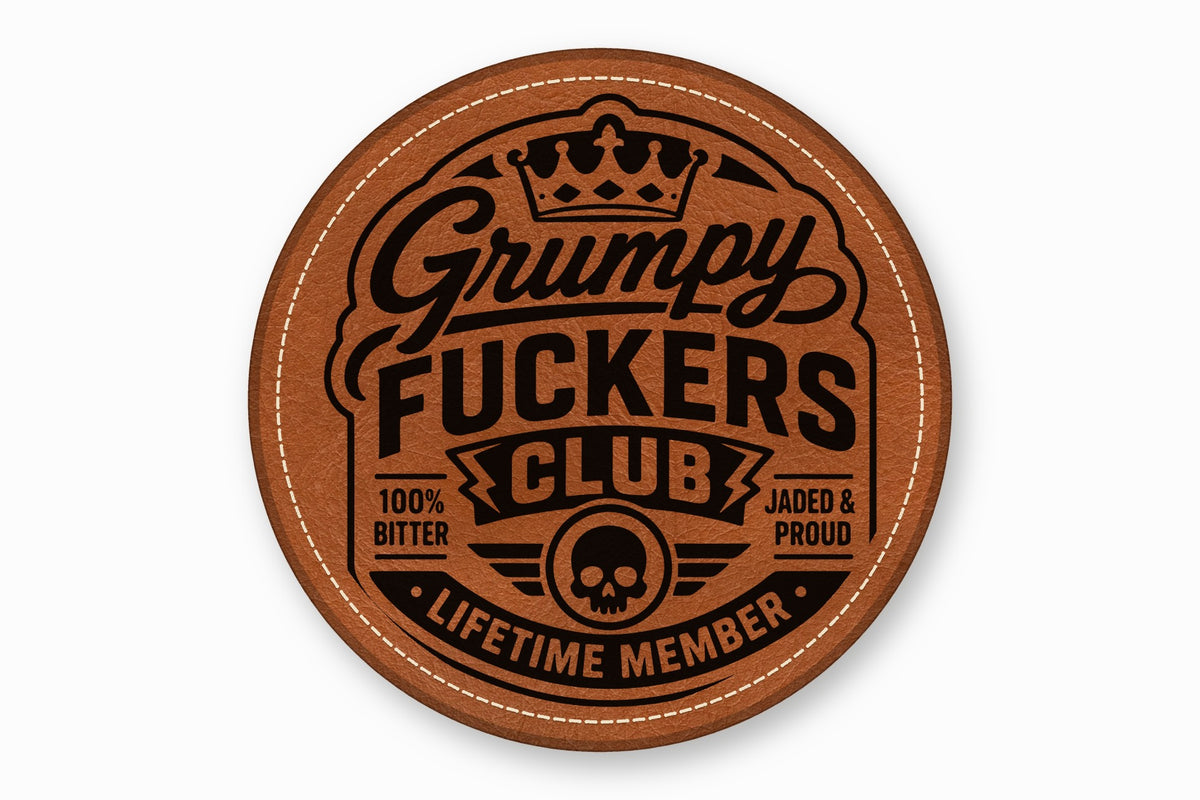 Round brown leather patch with white stitched border and black engraved text reading Grumpy Fuckers Club.