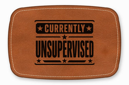 Brown leather patch featuring white stitching along the edge and black text reading Currently Unsupervised.