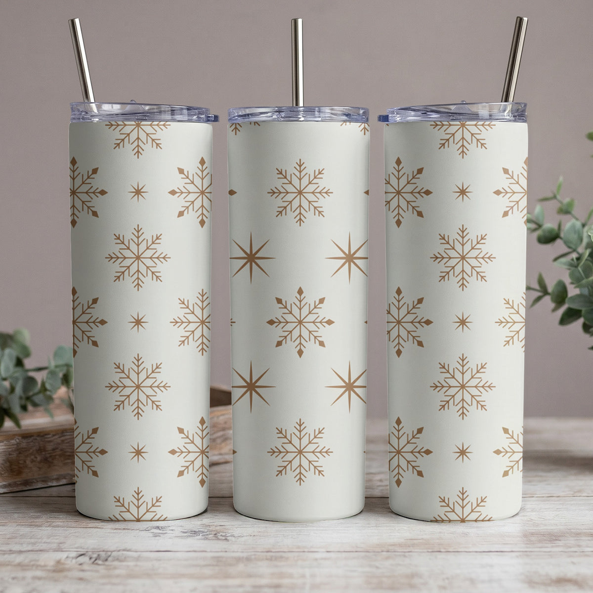 Three white tumblers with gold snowflake and star pattern and metal straws.
