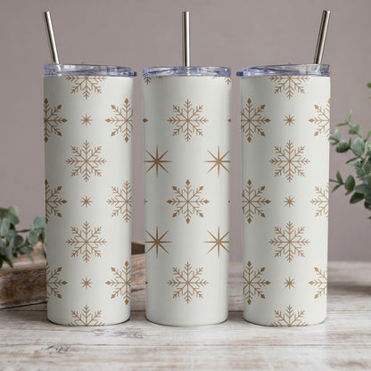 Three white tumblers with gold snowflake and star pattern and metal straws.
