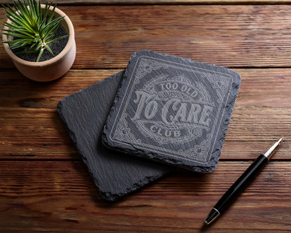 Engraved slate coaster reads "Too Old To Care Club" with a pen and plant.