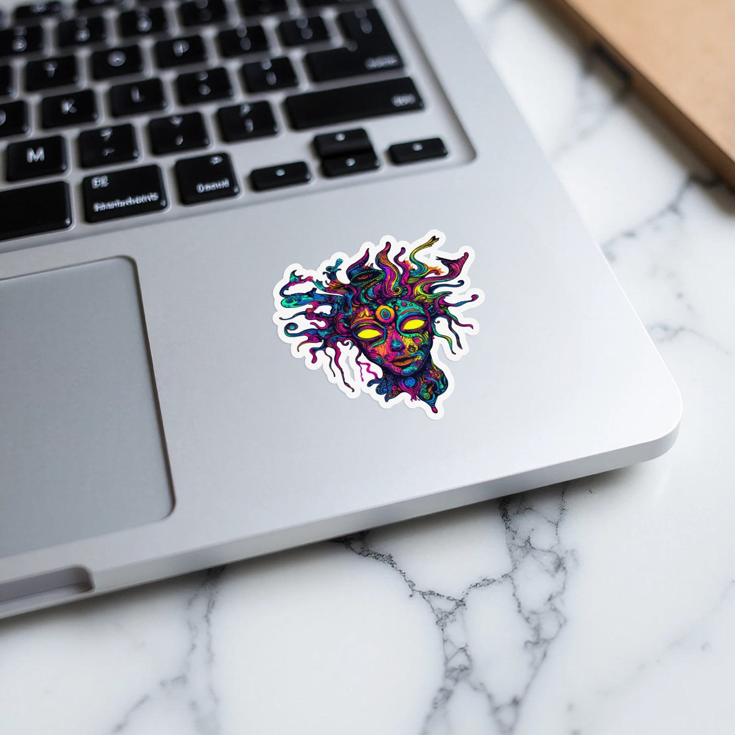 Psychedelic face sticker with yellow eyes on a laptop keyboard.