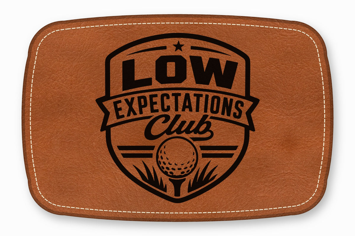 Brown leather patch featuring a black embroidered crest that reads Low Expectations Club with a golf ball.