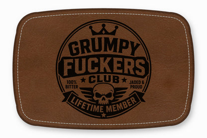 Brown leather patch with white stitched border and circular black text reading Grumpy Fuckers Club and Lifetime Member.