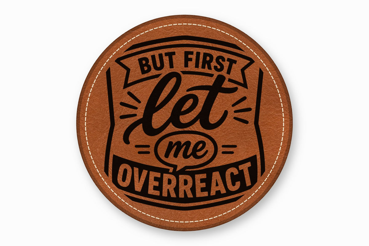 Round brown leather coaster featuring white stitched edges and black text reading BUT FIRST LET ME OVERREACT.